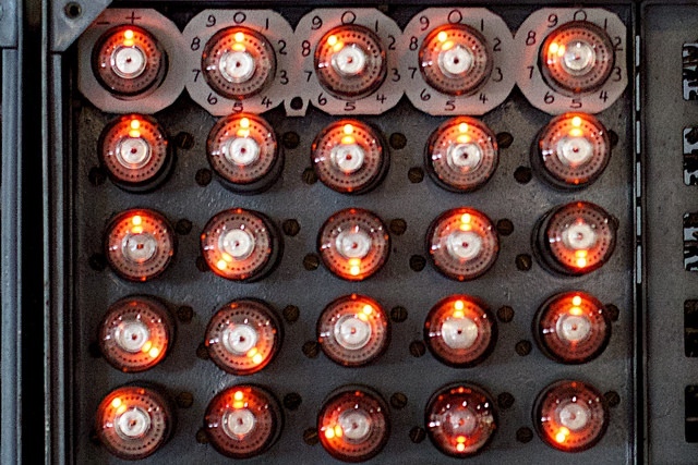 A 5x5 grid of “dekatrons”. Each dekatron has a series of black dots (the values), and a bright orange light showing the current value.